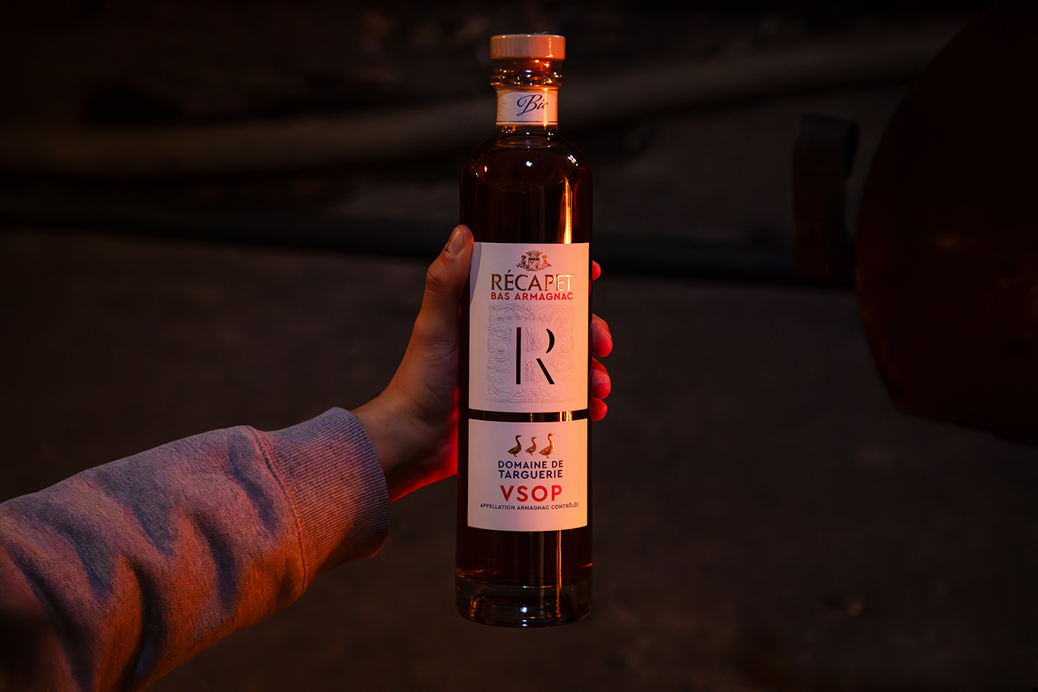 Bouteille d’Armagnac Récapet bio tenue dans une main, ambiance chaleureuse